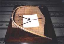 机の上に、供え物と3膳の箸がおかれた白い紙が乗った、大きな竹編みの農具が置かれている写真