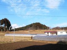 冬枯れの畑とビニールハウスが広がり、その奥に小さな集落と低い山がみえる押立館跡の写真