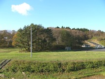 石段をのぼったところに広場がありその後ろに木々が茂り右奥には駐車場が見える広々とした景色を遠目から撮影した写真