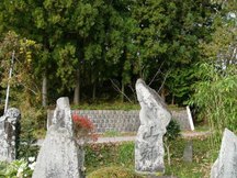 木々や竹が茂る斜面の下に、多数の自然石の石碑が並んでいる風景を捉えた写真