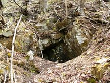 山中の斜面に岩を積み上げたような口が開き、奥が暗闇になっている坑口1/十枚山産金跡の写真