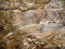 茶褐色の岩盤に白い鉱脈の筋が走っている様子を間近で撮影した坑道内壁/十枚山産金跡の写真