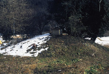 雪が部分的に残る丘の上に小さな石祠が建つ蝦夷塚の写真