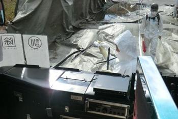 手前には大型の機械装置があり、その背後にはシートやブルーシートが地面を覆うように敷かれている様子の写真