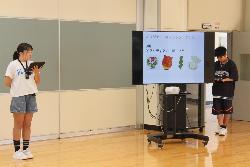 児童朝会でキャラクターのアイデアについて募集をする児童の様子