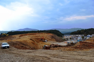 重機が盛土を整地しており、広く掘削された地面と遠くの建物群が見える志津川地区東工区造成工事の現場写真