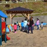 屋外の子ども用遊具エリアで、保護者と一緒に遊ぶ子どもたちが集まっている様子の写真