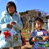 ふわふわのコートを着た女の子と男の子が笑顔でお土産を持っている写真