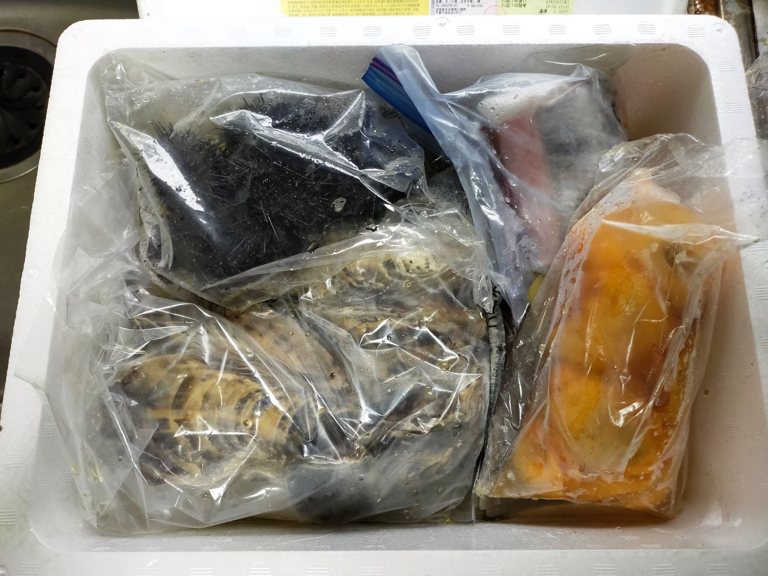 発泡スチロールの箱の中にウニや牡蠣、ホヤなどの魚介類が個別に袋詰めされて入っている写真