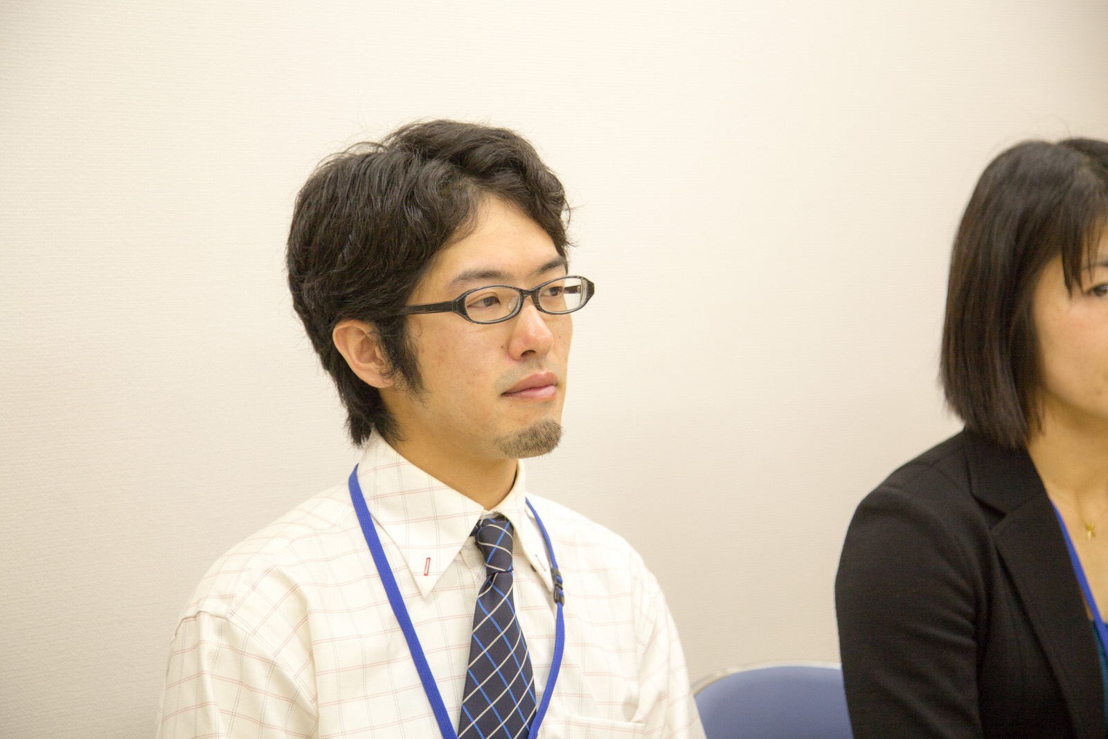 シャツとネクタイを着用し、眼鏡をかけた藤田さんが真剣な眼差しで前を見据えている写真