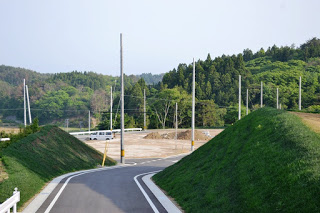 緩やかな坂を下る舗装道路の先に電柱と整地された土地が広がる住宅造成地の写真
