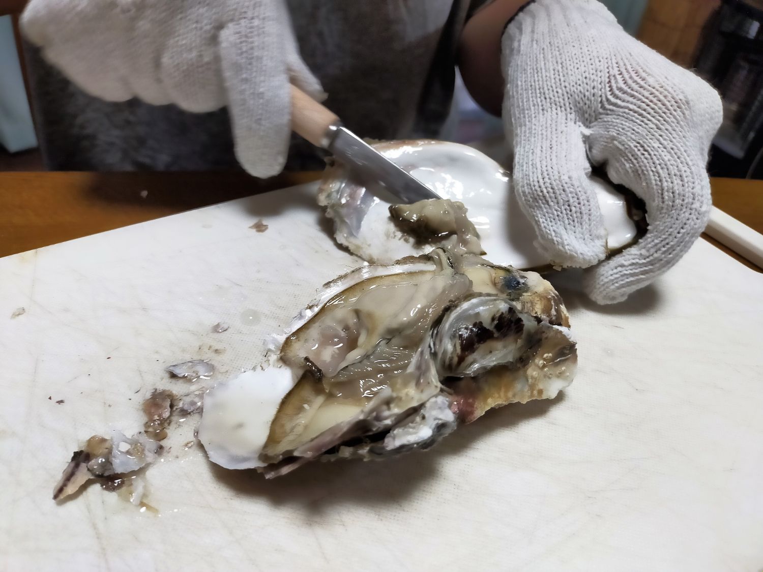 まな板の上で、開いた牡蠣の殻の中から中身を取り出している作業中の写真で、新鮮な牡蠣の身がはっきり見える写真