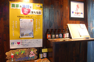 壁に取り付けられた瓶が飾られた飾り棚の左に「農家＆漁師と恋に落ちる店」と書かれた大きなポスターが貼ってある写真