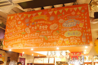 天井から設置されたオレンジ色のボードに、イラストを添えたたくさんのメニューが書かれている写真