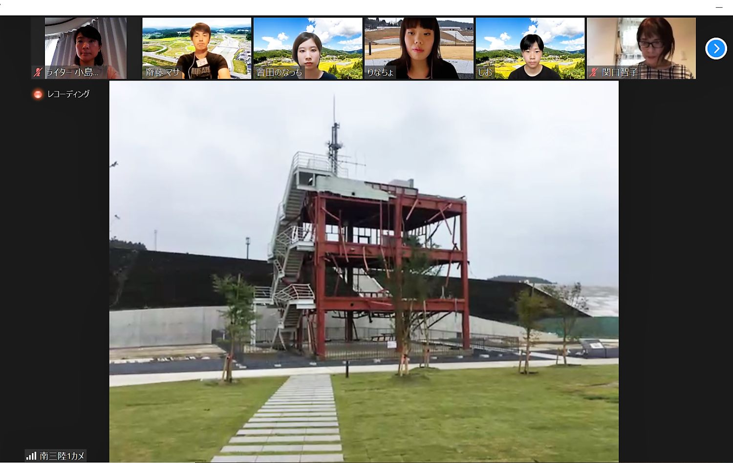 緑の芝生の前に幅広の石畳の道が続き、その先に鉄骨がむき出しで三階建ての階段や手すりが付いた赤茶色の防災対策庁舎をオンラインツアーの画面に映している写真