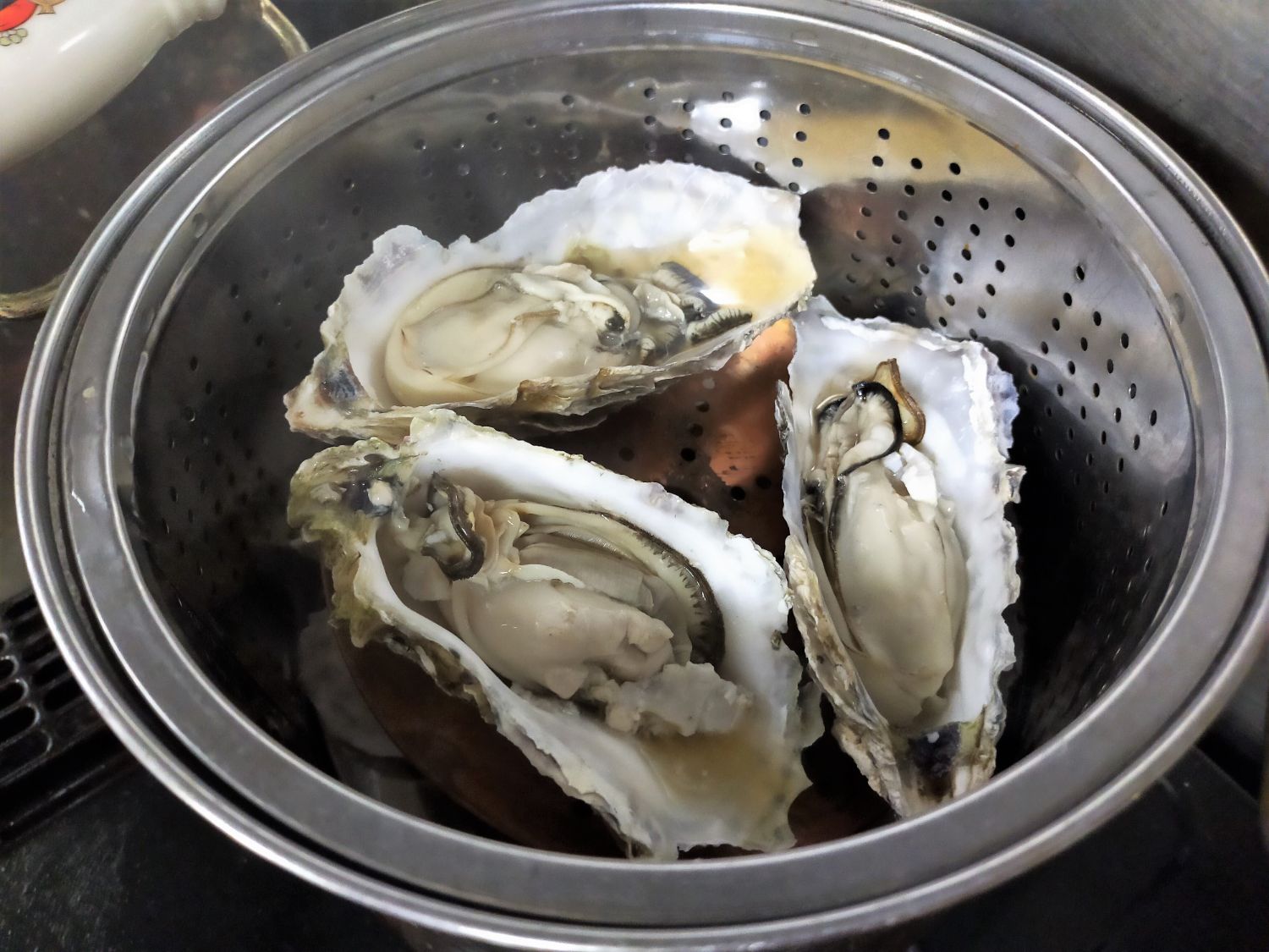 蒸し器の中に殻をあけた牡蠣が3つ入っており、加熱調理中であることがわかる蒸し牡蠣の写真