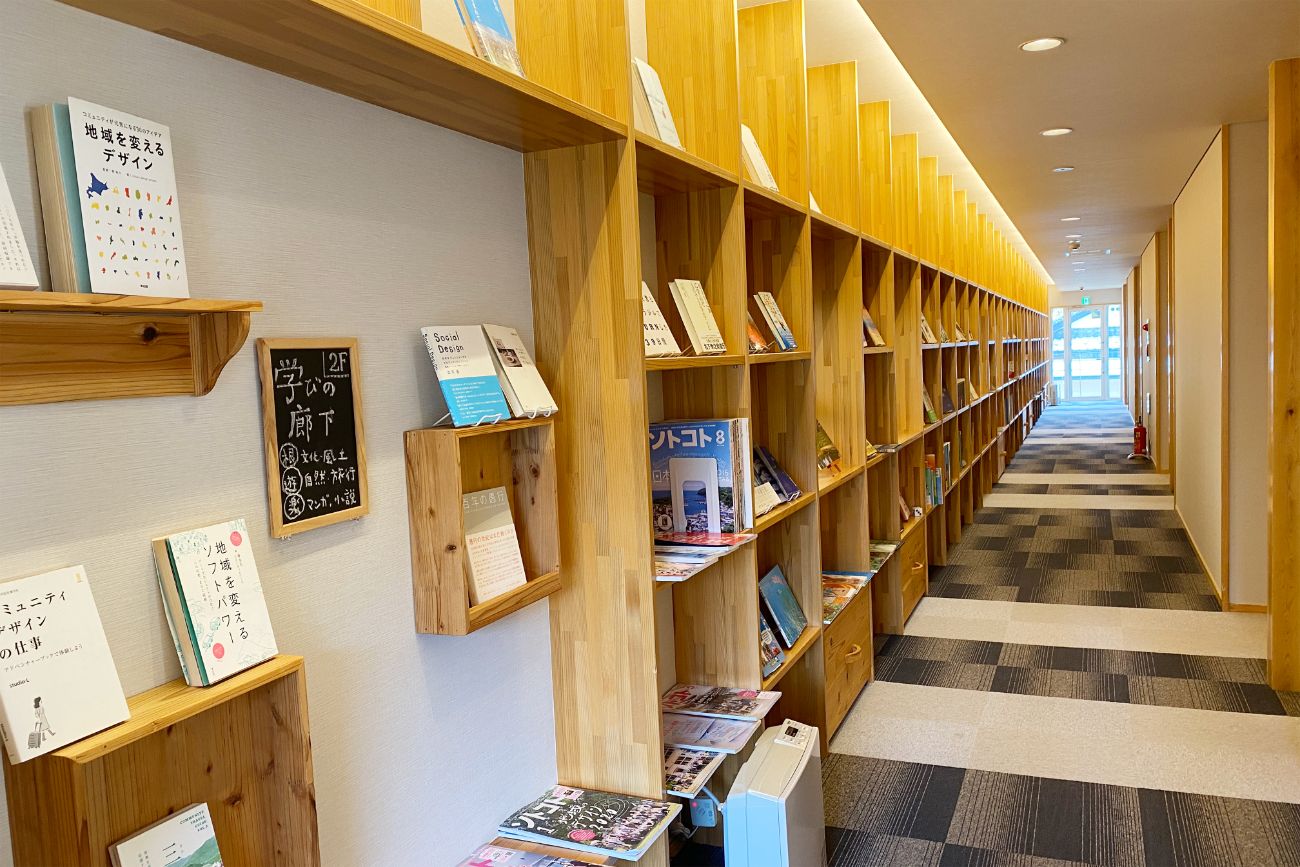 長い廊下の左側の壁に木の棚が並び、様々なジャンルの多くの本が展示されている学びの廊下の写真
