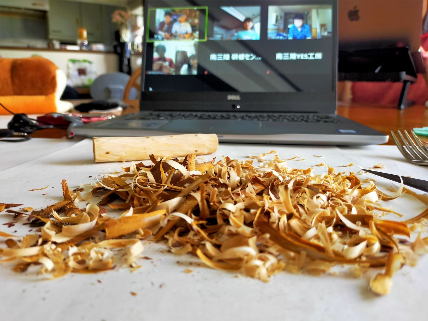 テーブル上に削り終えた杉枝が置かれ、その前にたくさんの削りカスが散らばり、奥にオンラインワークショップ画面のノートパソコンが置かれている写真