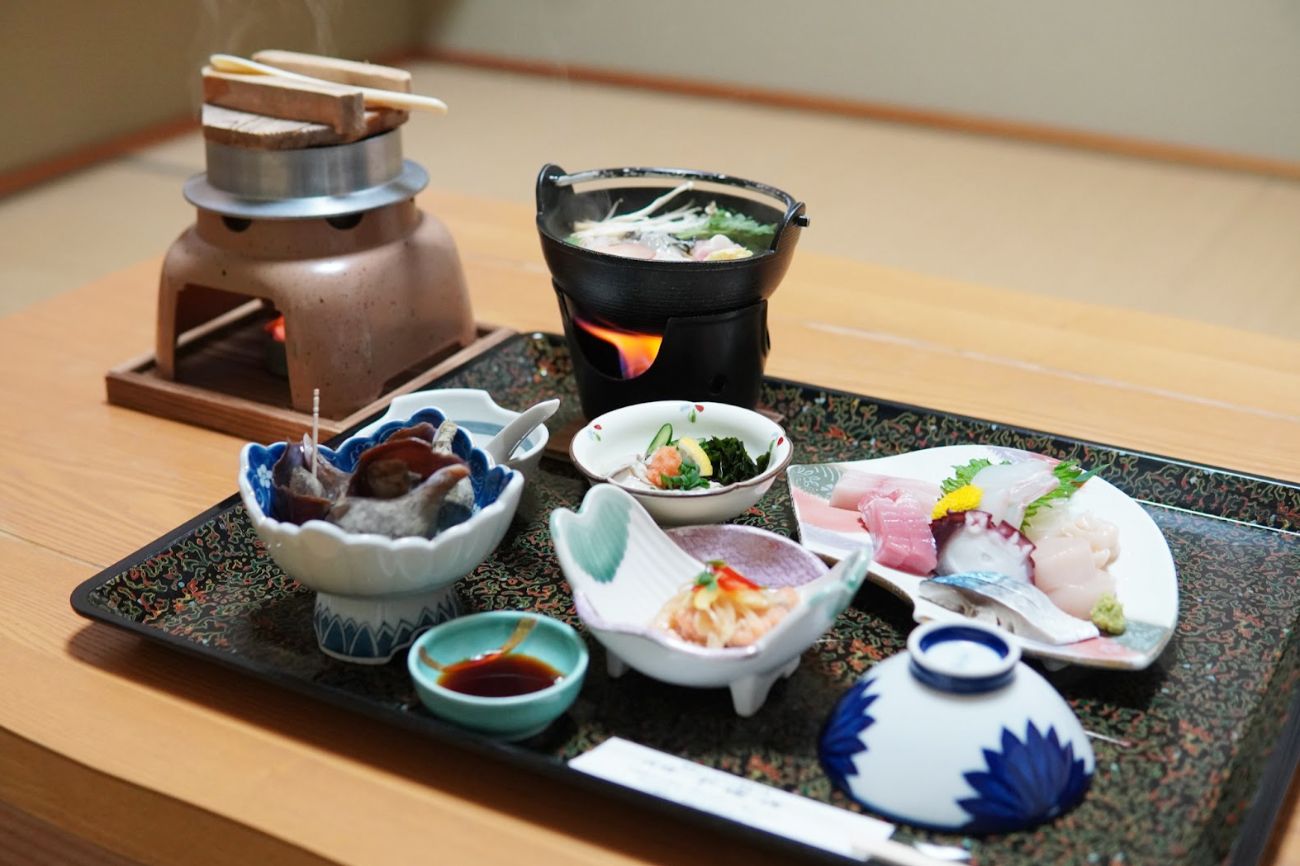 和風の机の上に、釜で炊いたご飯、刺身や鍋、小鉢などが並んだ豪華な和定食の写真