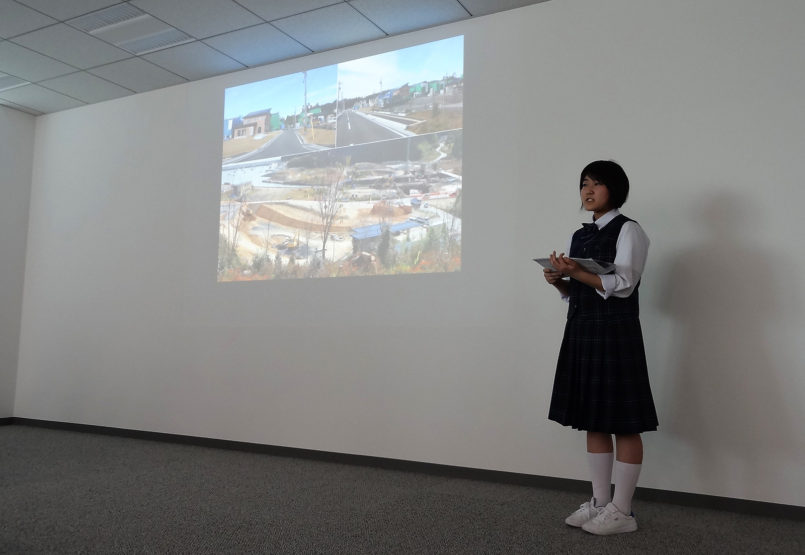 女子生徒が、震災後の復興の様子の写真が投影された壁の前に立ち、発表をしている写真