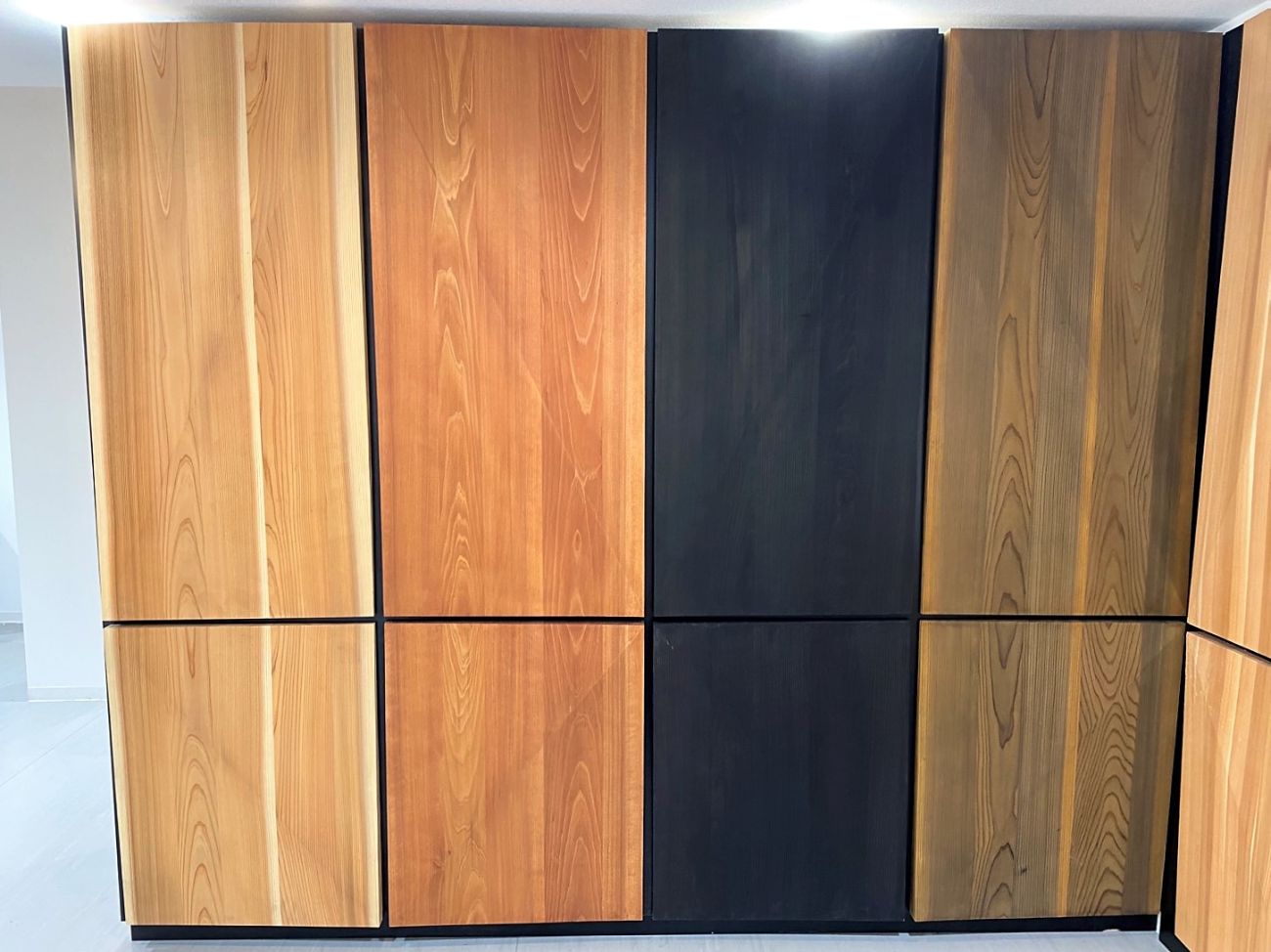 木目が異なる四種類の木材、明るい黄褐色、やや濃いオレンジがかった茶色、黒色、暗めの茶色のサンプルが並んでいる写真