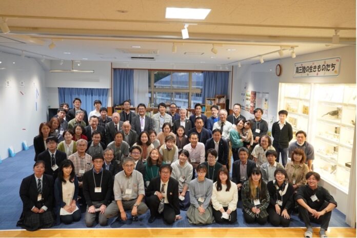 「南三陸いのちめぐるまち学会」の参加者が何列にも分かれて並び、カメラに向かって笑顔で写っている集合写真