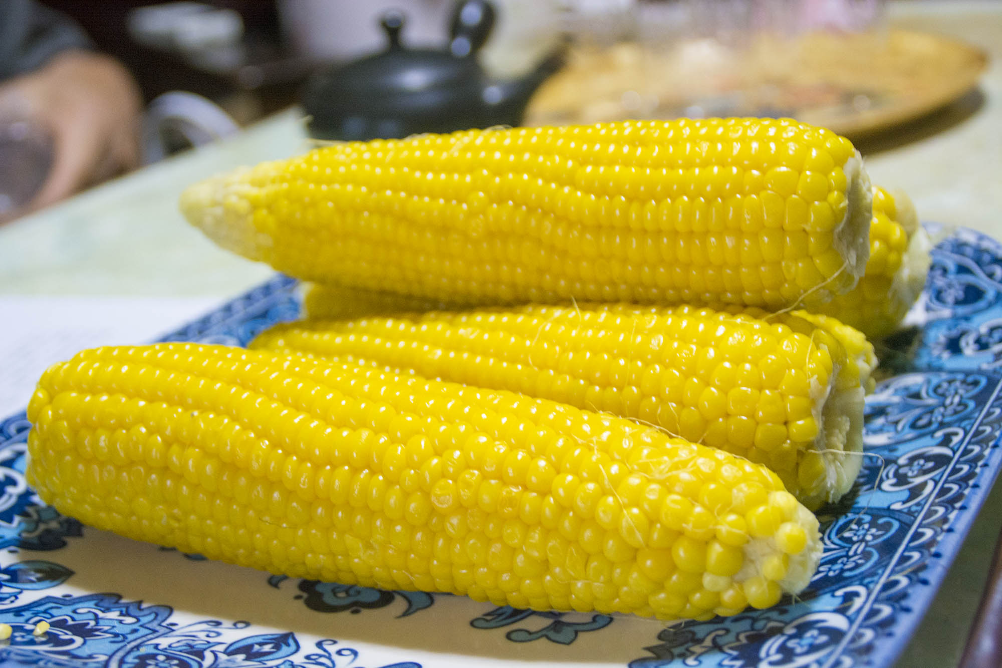 青い絵柄の四角い皿に黄色い身がぎっしり詰まったゆでトウモロコシが数本乗っている写真
