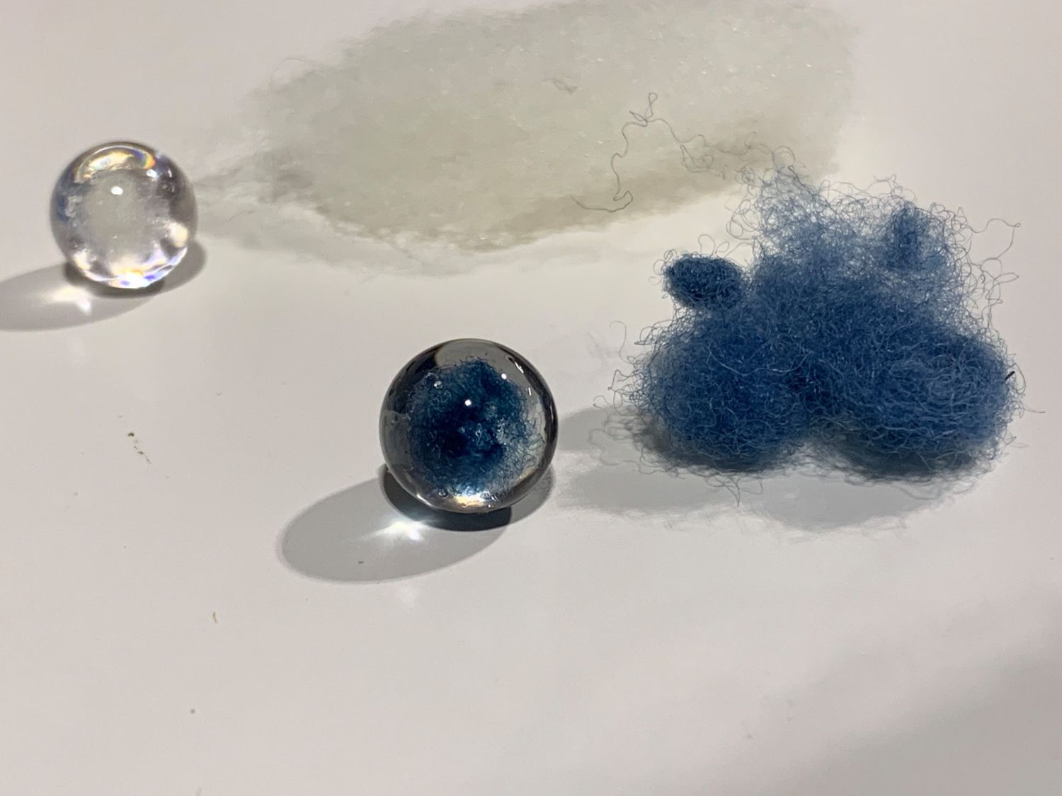 白と青の繊維のかたまりのそばに、透明と青色の2つの球体が置かれている写真で、球体の内部に繊維状の模様が見える写真