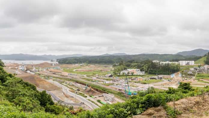 曇り空の下、広大な造成地を見下ろす定点カメラによる風景で茶色く盛られた土の山や削られた斜面が連なり、工事中の道路や造成区画が続き中央には複数のクレーンや建設重機が並び、基礎工事やインフラ整備が進められている様子の写真