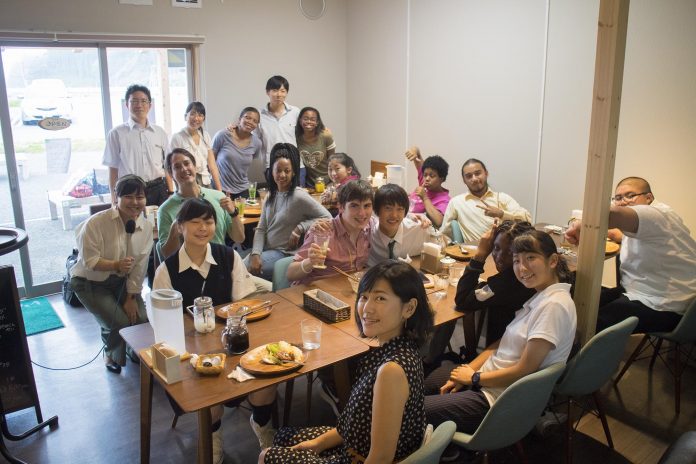 たくさんのアメリカと日本の学生たちがカフェの店内で料理が置かれたテーブルを囲みながら笑顔でポーズを取っている記念写真