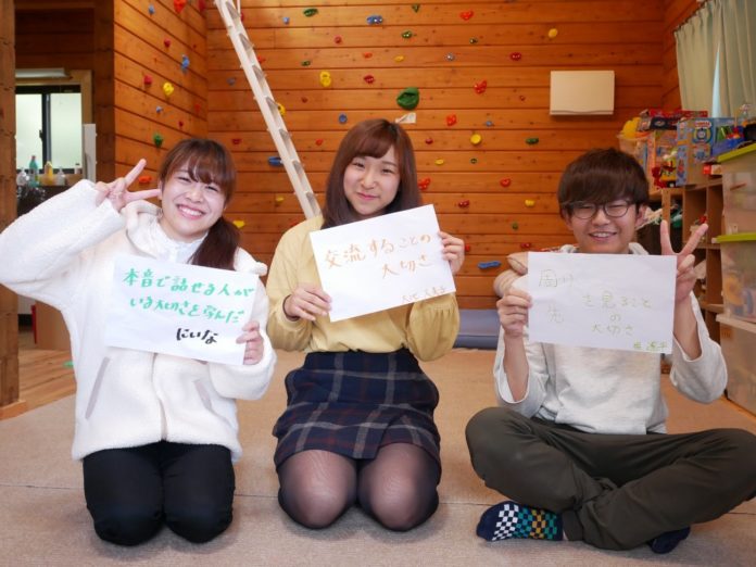 3人の学生が室内でそれぞれ手書きのメッセージを持って座っている写真