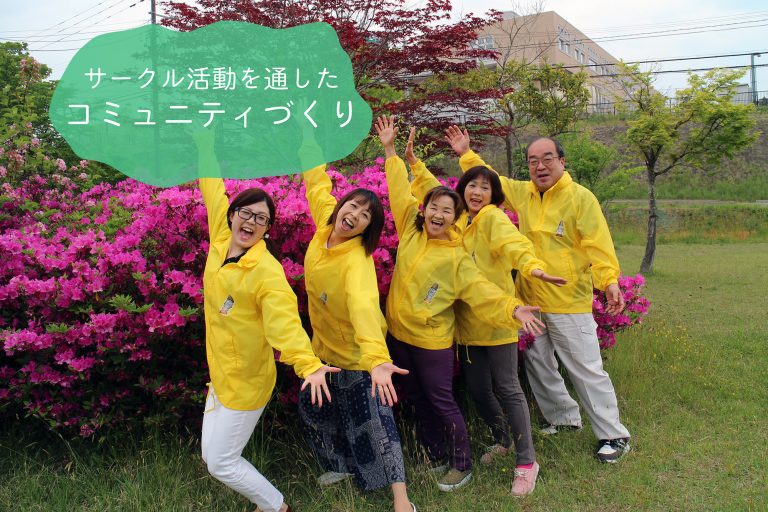 ピンク色のツツジの前で黄色いジャンパーを着た地域住民6人が笑顔で手を上げてポーズをとっており、上には「サークル活動を通したコミュニティづくり」という文字が表示されている地域活動紹介の写真