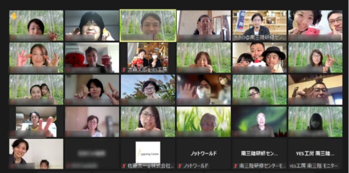 ビデオ会議のギャラリービューで、全ての参加者の顔が一画面に並び、それぞれが笑顔でピースサインをしたり手を振ったりしているオンライン会議の様子を写した写真