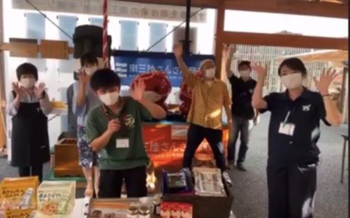 沢山の特産品の商品が陳列されている店内で、6人がカメラに向かって手を振っている「バーチャルまちあるき語り部×オンラインショッピング」動画のスクリーンショット画像