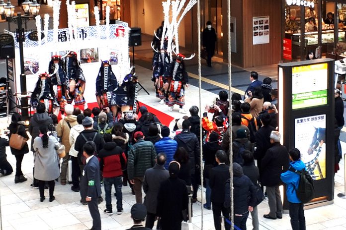 伝統衣装を着た南三陸町の鹿踊りが、商業施設内の特設ステージで大勢の観客を前に披露されている様子の写真