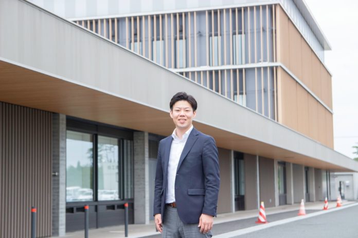 新しくて現代的なデザインの建物の前に笑顔で立っているスーツを着た男性の写真