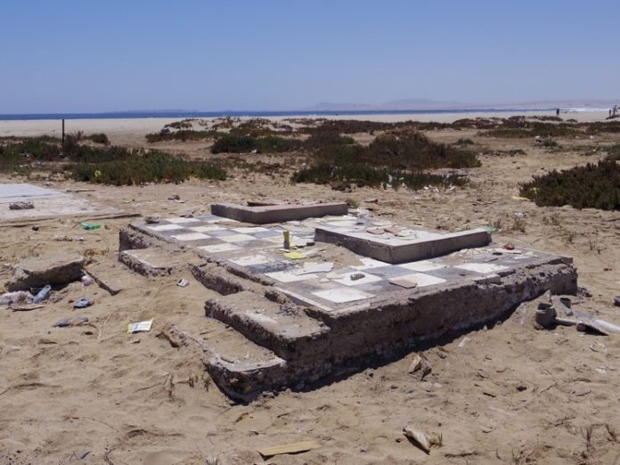 砂浜に古くなったチェス盤のようなコンクリートの基礎部分が取り残されている写真