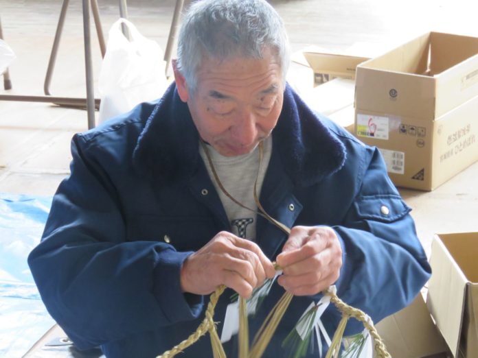 紺色のジャンパーを着た佐藤和行さんが真剣な表情で縄を編んでいる様子の写真