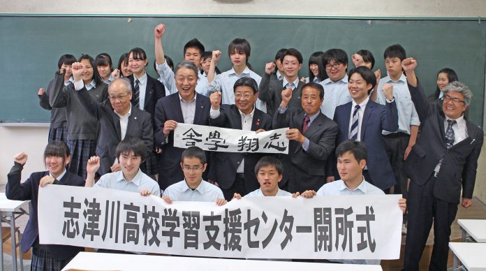 教室の黒板の前で、多くの高校生や関係者の方々が笑顔で拳を上げ、「志津川高校学習支援センター開所式」と書かれた横断幕を持って記念撮影している写真