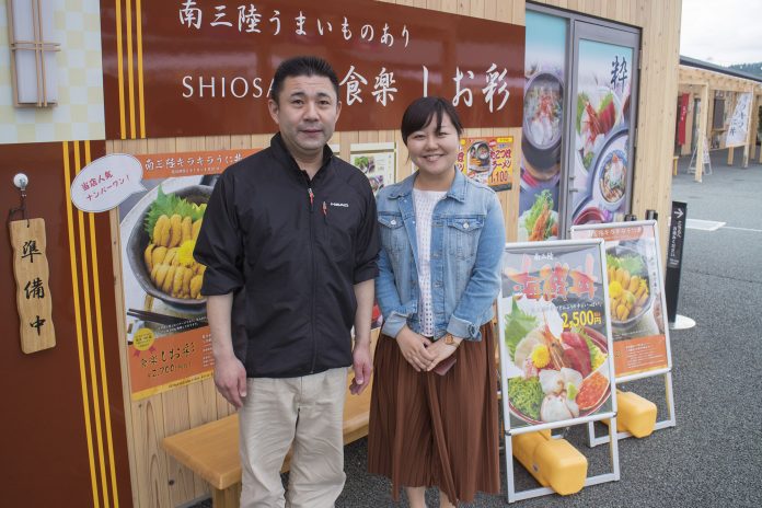 「食楽しお彩」と書かれた茶色の看板やたくさんの料理のポスターが貼られた店舗の壁の前に並んで立った後藤さんと女性リポーターの写真