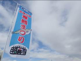 冬空の下、「寒鱈まつり」と書かれ、タラのイラストが描かれた水色ののぼり旗が風にはためいている様子の写真