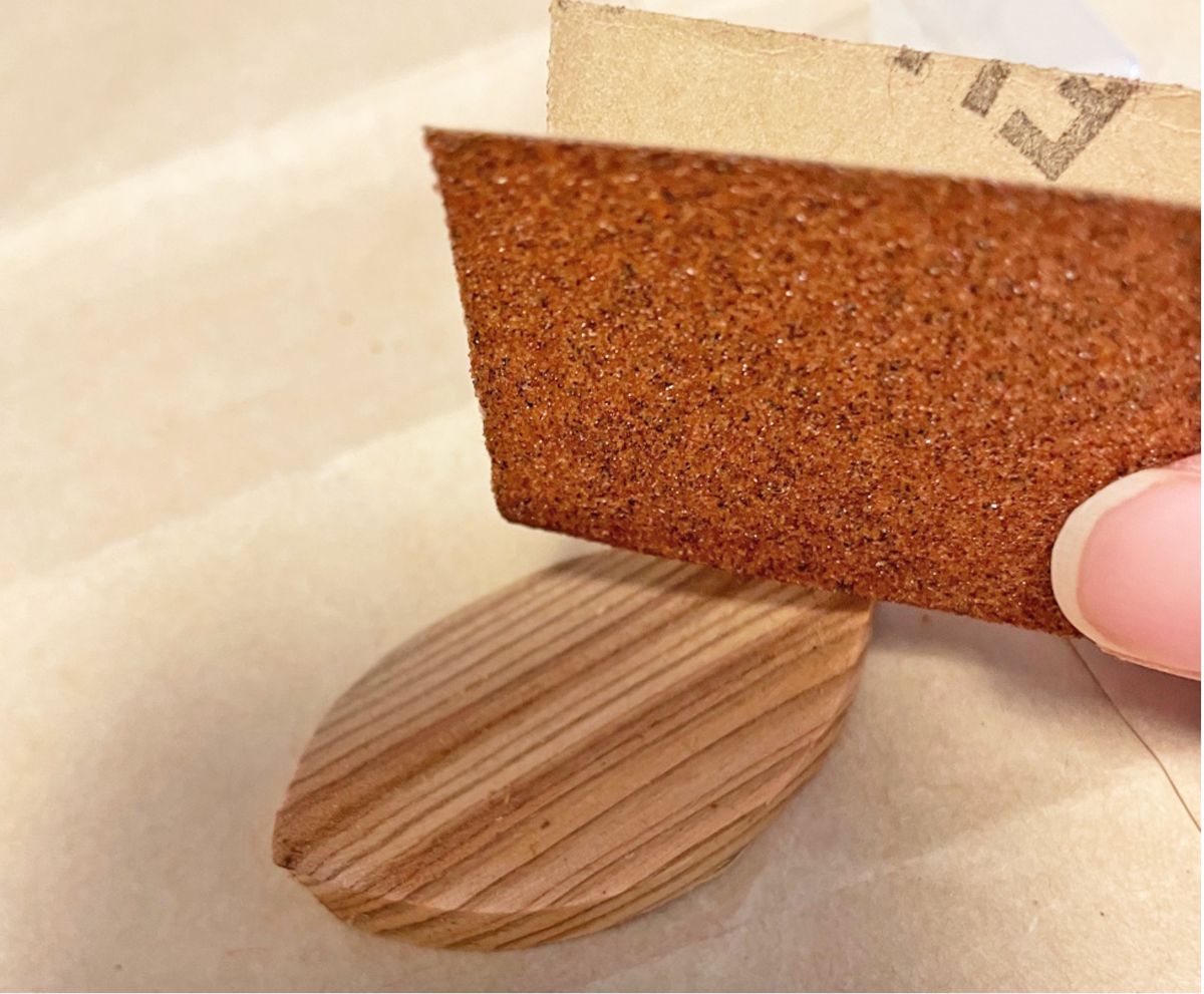 手に持った茶色の紙やすりで、葉っぱの形をした木のパーツの表面をこすって磨いている写真