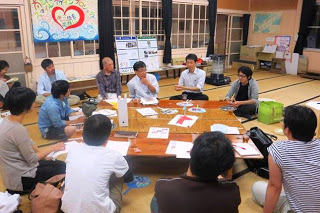 和室の部屋で複数の参加者が座卓を囲み、資料を見ながら真剣に話し合いをしている写真