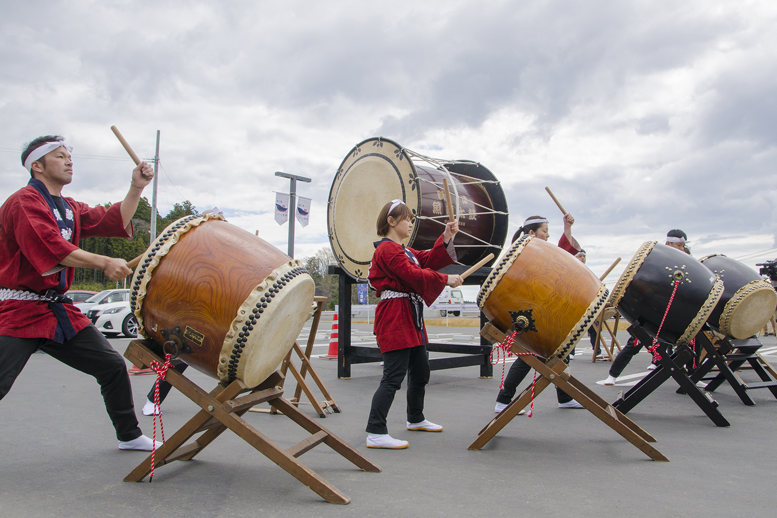 屋外で赤い法被姿の演者たちが大きな和太鼓を力強く演奏している写真