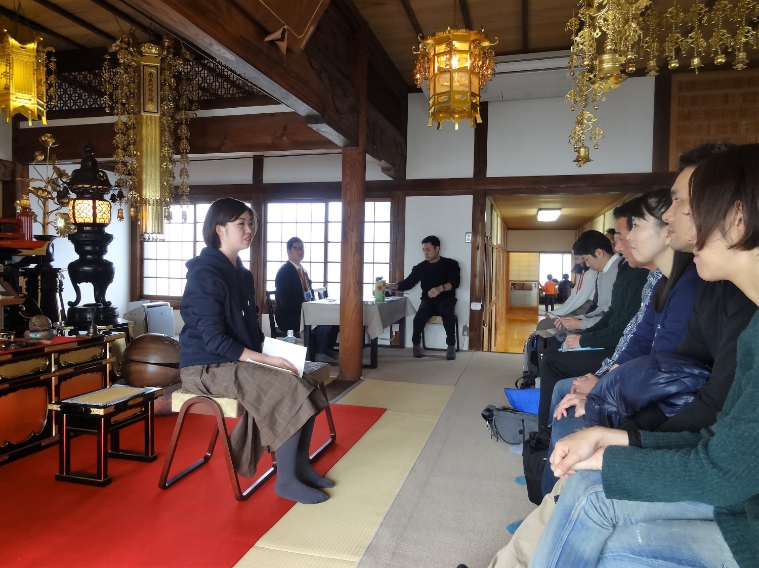 お寺の本堂で数人の人々が整然と座り、前方の話し手に耳を傾けている様子が写されている写真