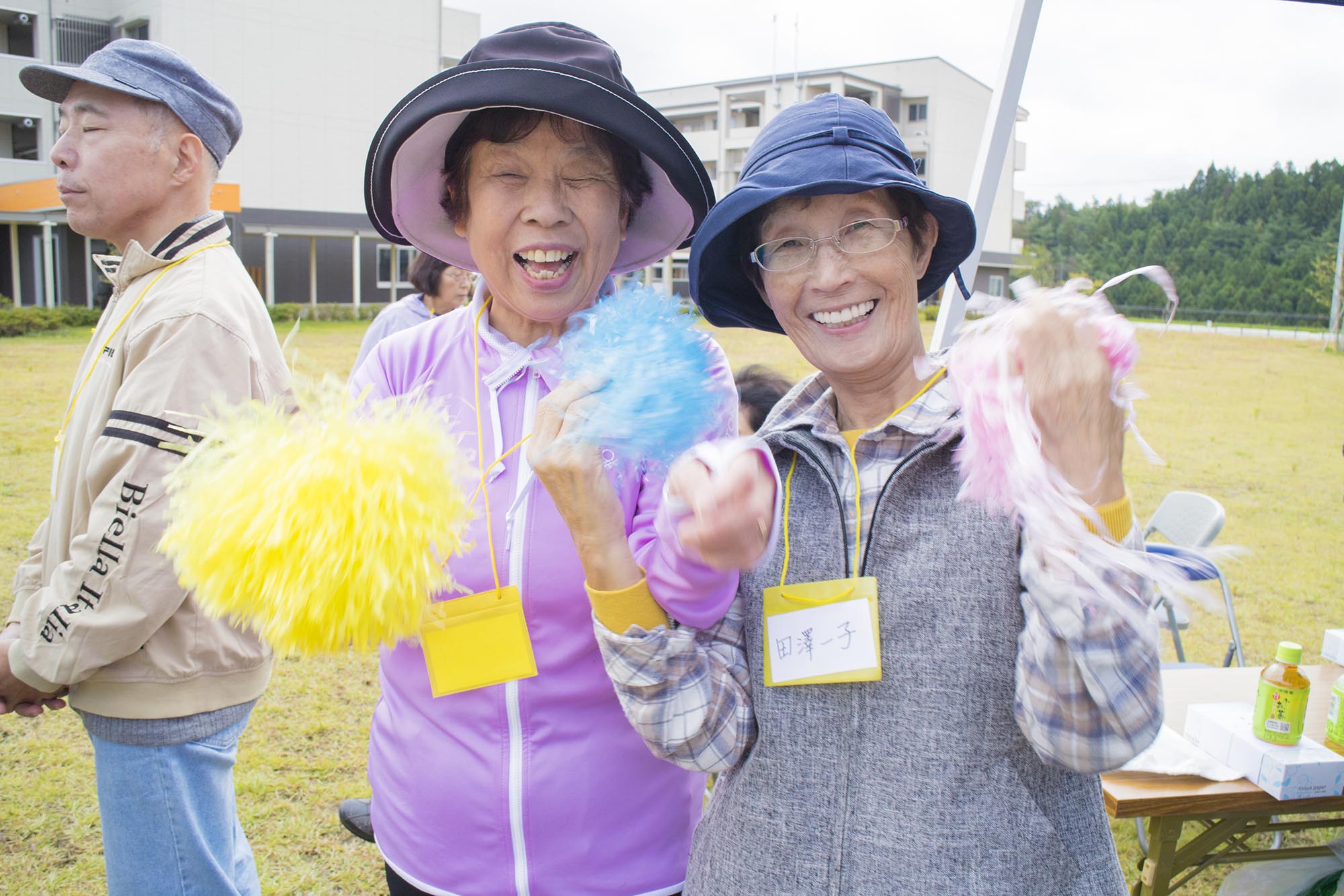 女性2人がそれぞれカラフルなポンポンを持ってカメラに向かって笑っている写真