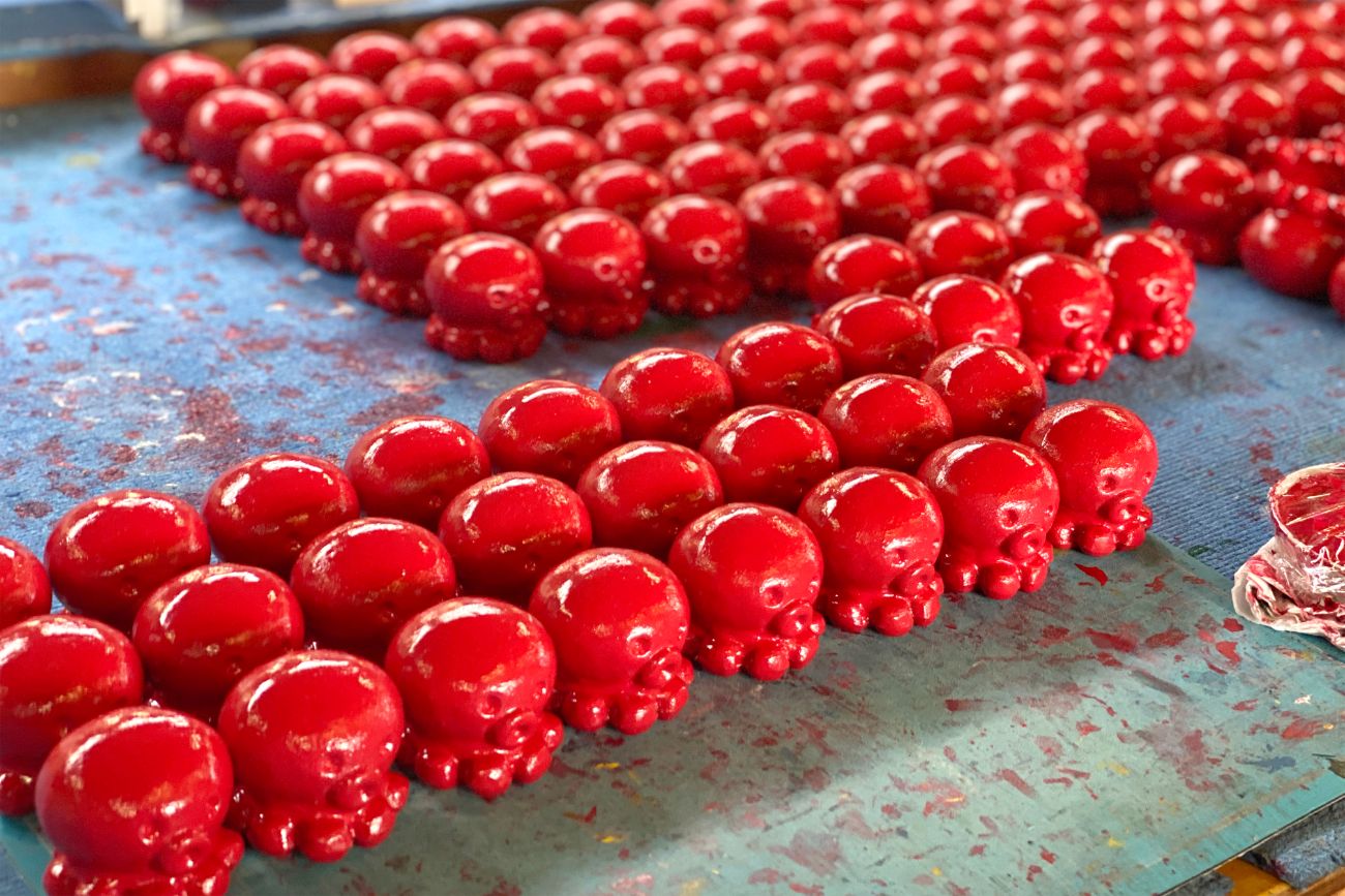 赤く塗装されたタコの形をしたオクトパス君の小さな置物が整然と並べられて乾かされている工房の写真