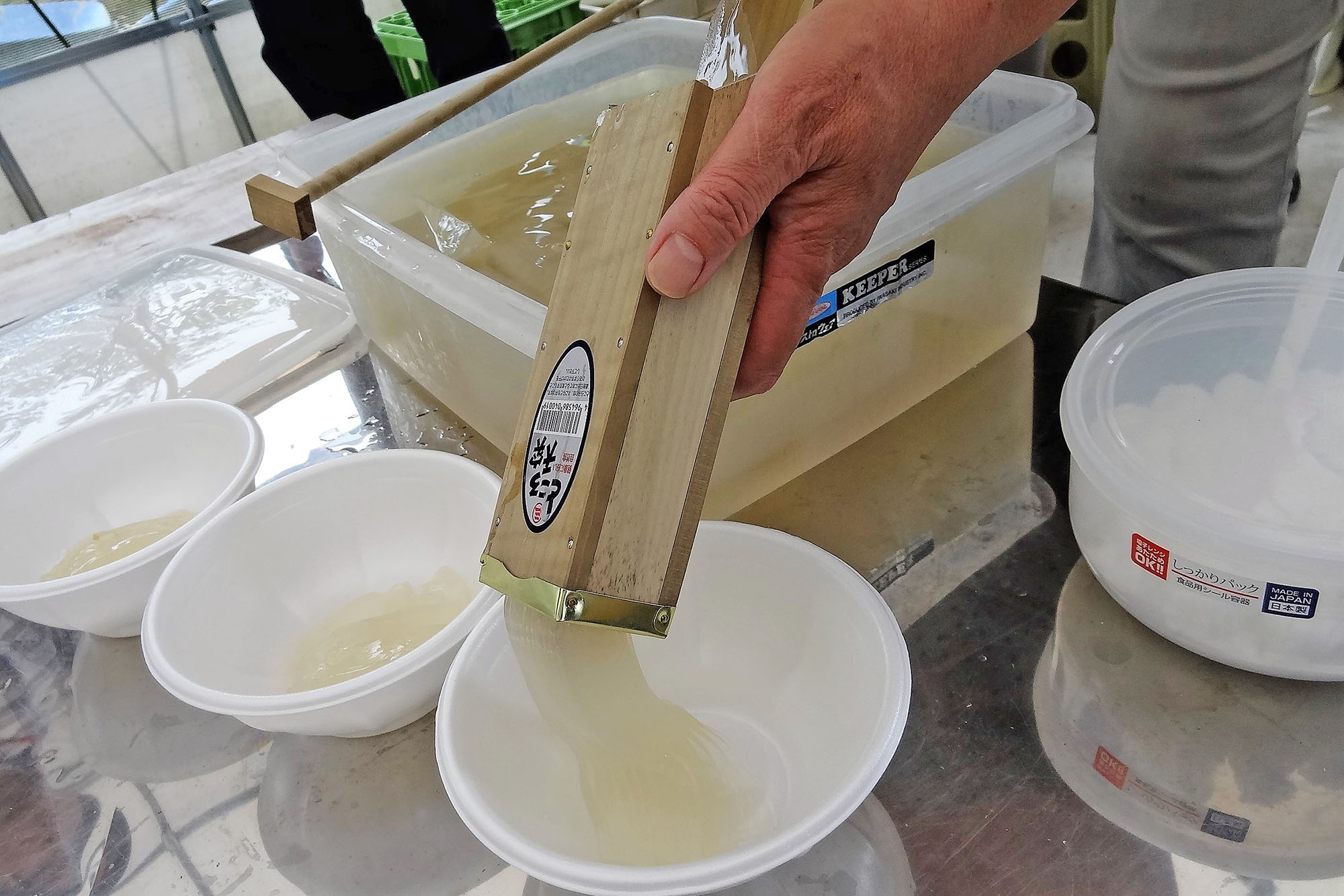タッパにーに入ったところてんを箱状の容器に入れ、突き棒で押し出し丸い白いどんぶりに押し出している写真