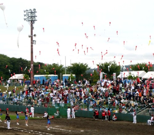 観客席を埋め尽くした大勢の観客が、多数の赤い細長い風船を一斉に空へ解放しているプロ野球イースタンリーグ公式戦の様子の写真
