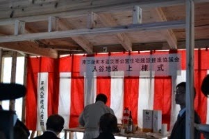 紅白幕が張られた建築中の建物の中で、神棚とお神酒が供えられた祭壇の前に作業服姿の男性が立っている、上棟式の神事が行われている祭壇の写真